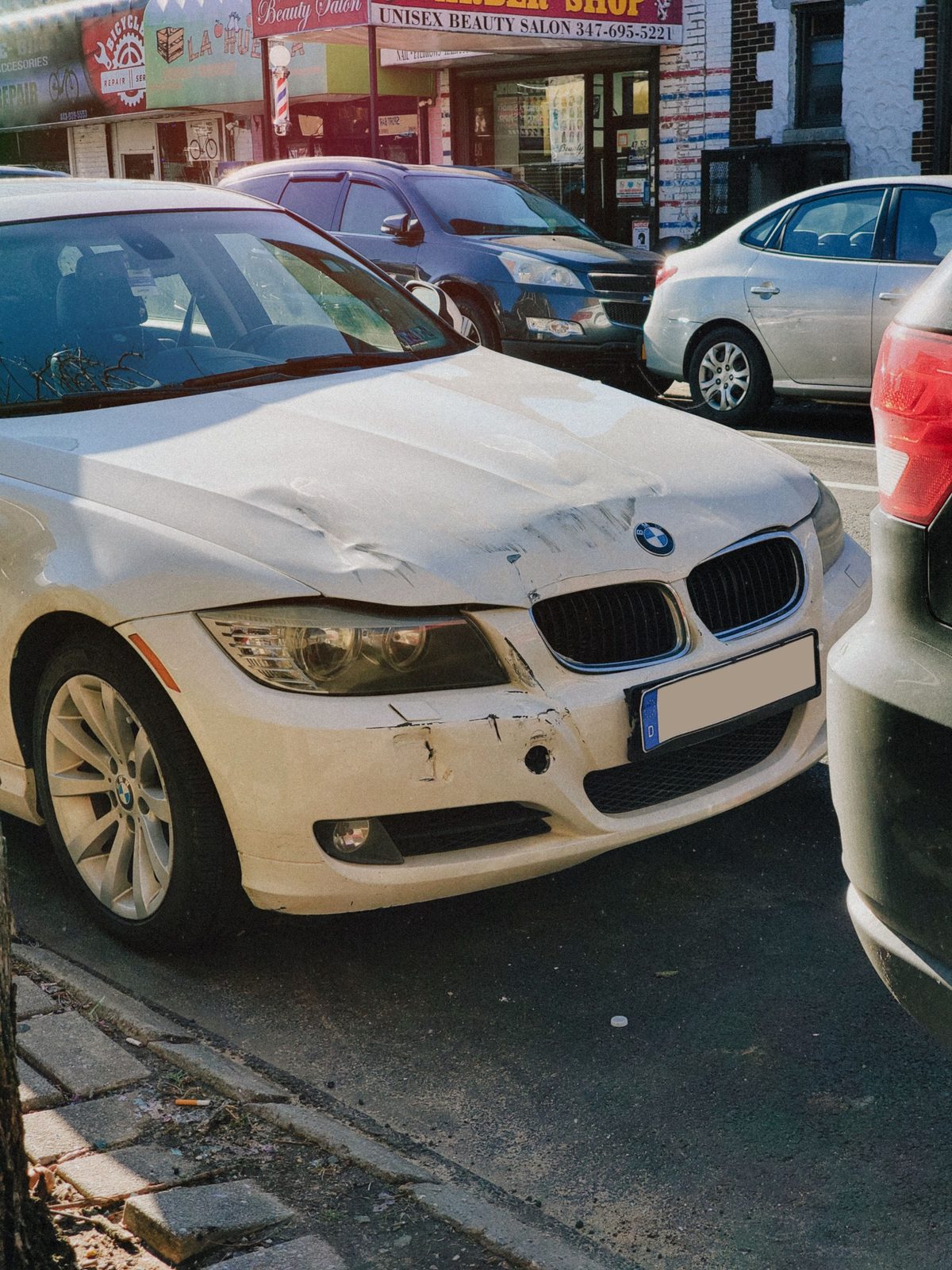 White car with front-end damage parked on a street after a collision